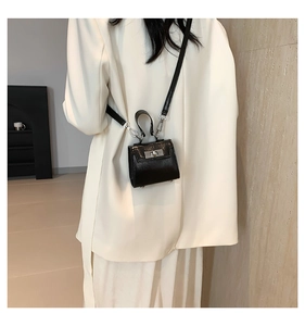Miniature black crossbody bag with metallic lock shown on a model in a modern interior