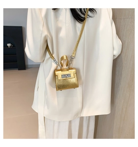 Detail of a mini gold metallic bag with a twist lock closure on a white blazer outfit