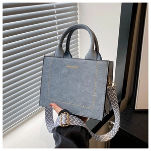 Detail van grijsblauwe suède handtas met geometrische brede riem en modieuze tekst