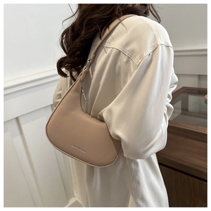 Detail view of crescent hobo bag in beige leather texture worn by a model indoors