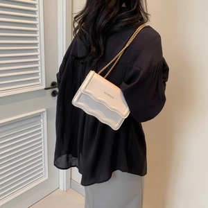 Minimalist white leather crossbody bag with wavy texture and gold chain strap on model