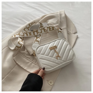 Detail of white V-quilted crossbody bag with golden deer pendant on a beige blazer