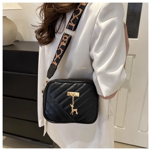 Détail du sac bandoulière matelassé noir avec pendentif cerf doré et sangle imprimée