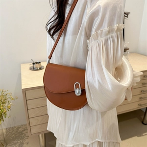 Sac bandoulière chic en cuir marron avec boucle argentée porté par un modèle