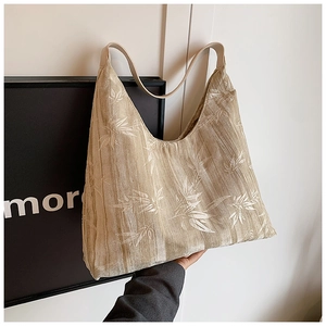 Close-up of beige shoulder bag with white leaf patterns and leather straps in hand