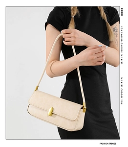 Close-up of beige rectangular baguette bag with a golden oval metal clasp and strap