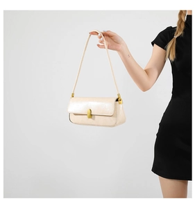 Detail of cream-colored glossy leather underarm bag with gold oval clasp and hardware