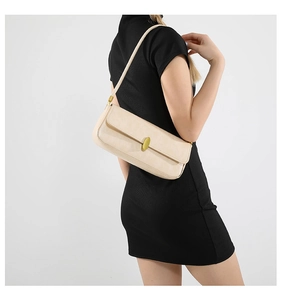 Detail of a beige leather baguette bag featuring a gold oval clasp and slim shoulder strap
