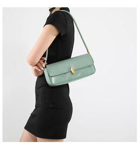 Detail of sage green underarm bag with gold oval clasp worn by a model in black