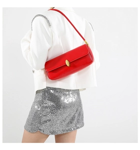 Red glossy leather underarm bag with gold oval clasp worn on white suit for styling
