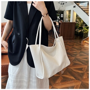 Close-up of white oversized tote bag featuring crocodile embossed texture and slim handles