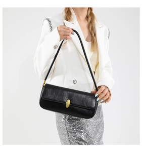 Close-up of elegant black baguette shoulder bag with gold oval clasp on white blazer
