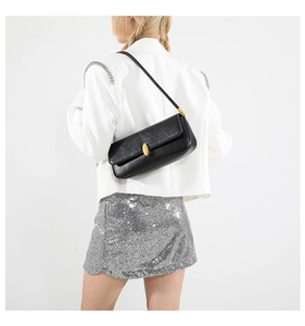 Rear view of a black leather baguette bag with a gold oval clasp on a white suit model