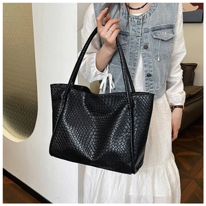 Close-up of a large black woven tote bag showing detailed texture on a fashion model