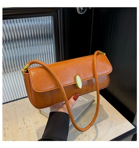 Detail of tan leather baguette bag with elegant golden oval metal clasp and slim strap