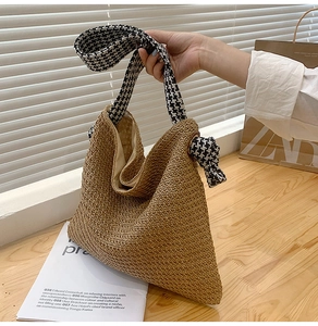 Close-up of woven straw tote bag with houndstooth patterned fabric strap and metal eyelet