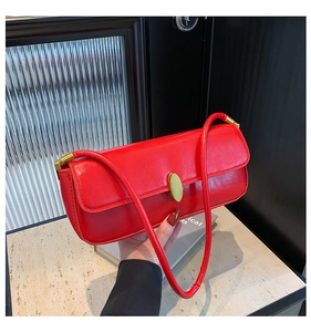 Detail of red glossy shoulder bag with a gold oval buckle on a marble surface