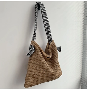 Detail of woven straw bag with black and white houndstooth knotted strap on white wall