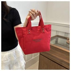 Detail of red canvas tote bag featuring black letter print and silver rivet reinforcement