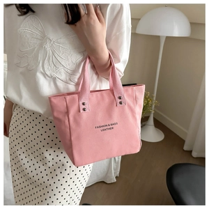 Pink canvas tote bag with black lettering and reinforced handles in a cozy home setting