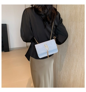 Detail of light blue flap bag with gold SSS logo buckle and tassels on model