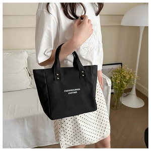Detail shot of black canvas tote bag showing white fashion letter print and metal rivet handles
