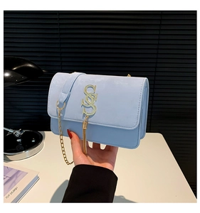 Close-up of light blue shoulder bag with golden S-shaped buckle and long fringe tassel