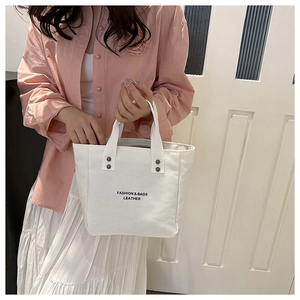 Detailed macro view of white canvas tote with black lettering and reinforced rivet handles