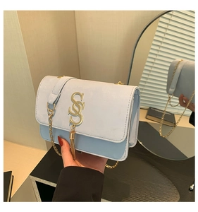 Close-up of light blue suede shoulder bag with gold S-buckle and tassel detail