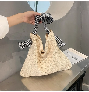 Detail der gewebten Strohhandtasche mit Hahnentritt-Henkeln und dekorativen Schleifen