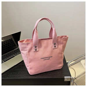 Pink canvas tote bag detail featuring black text print and silver rivet handles on a desk