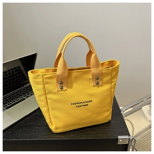 Close-up of yellow canvas tote bag with metal rivets and black slogan on wooden table