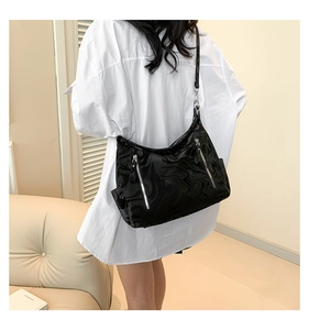 Detail of high-gloss black shoulder bag with silver zipper on a casual model outfit