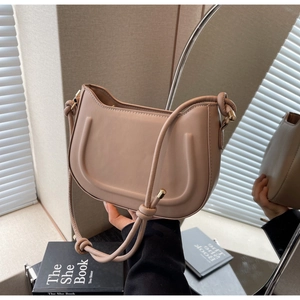 Detail of light apricot leather bag featuring U-shaped embossing and knotted strap hardware