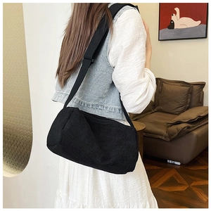 Detail of black corduroy shoulder bag with adjustable wide strap shown on a model