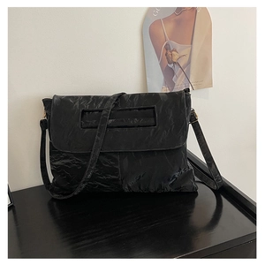 Detail of black wrinkled texture flap bag featuring a rectangular cutout handle and strap