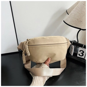 Détail du sac de poitrine beige avec bandoulière large et pendentif tressé