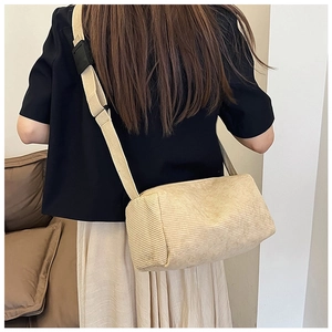 Back view of a beige corduroy cylinder crossbody bag on model with wide strap