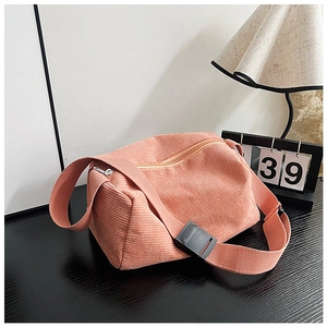 Detail of coral corduroy crossbody bag texture and wide adjustable strap on a dark table