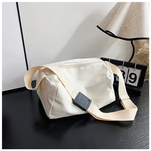 Detail of white corduroy crossbody bag featuring a textured finish and black buckle strap