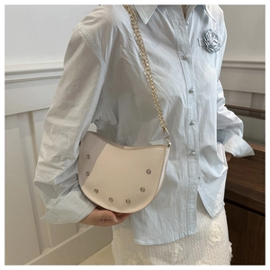 Detail of white half-moon shoulder bag featuring gold chain and metal rivet studs