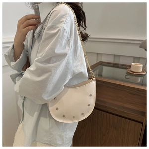 Detailed close-up of ivory crescent bag with silver rivets and golden chain strap