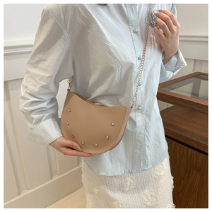 Detail of beige saddle bag with metallic studs and a delicate gold chain shoulder strap