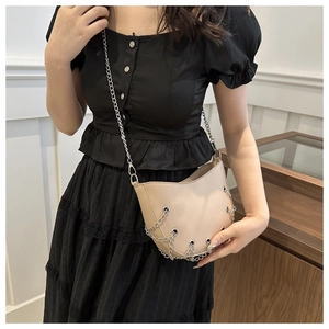 Chic beige crossbody bag with decorative silver chains and metal eyelets on model
