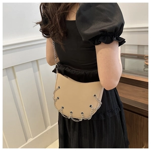 Detail of beige crescent shoulder bag with metallic eyelets and layered chain decoration