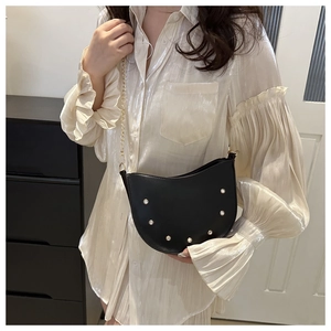 Detail of black faux leather crescent saddle bag with pearl rivets and gold chain