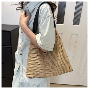 Detail of hollow-out straw tote with black leather straps on a model's shoulder