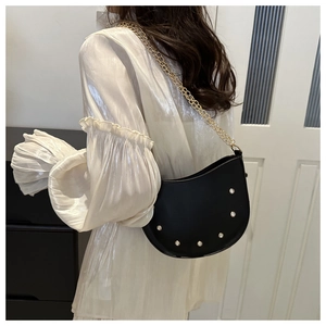 Detail of a black matte leather saddle bag with pearl studs and golden chain strap