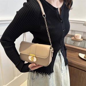 Chic beige crossbody bag with gold T-lock and chain strap shown on a female model