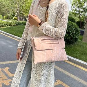 Pink glossy faux leather crossbody bag with top handle shown in an outdoor setting